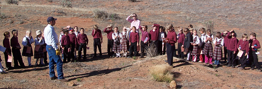 Group of students and two adults stand outside