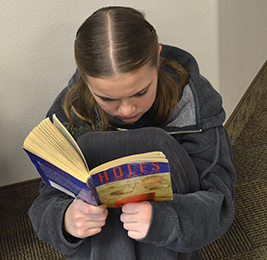 Female student reads the book Holes as she sits on the floor