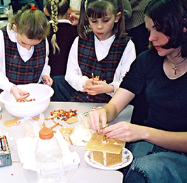 Staff member makes a gingerbread house with two students