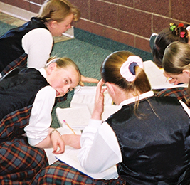 Students work on classwork as they sit on the floor